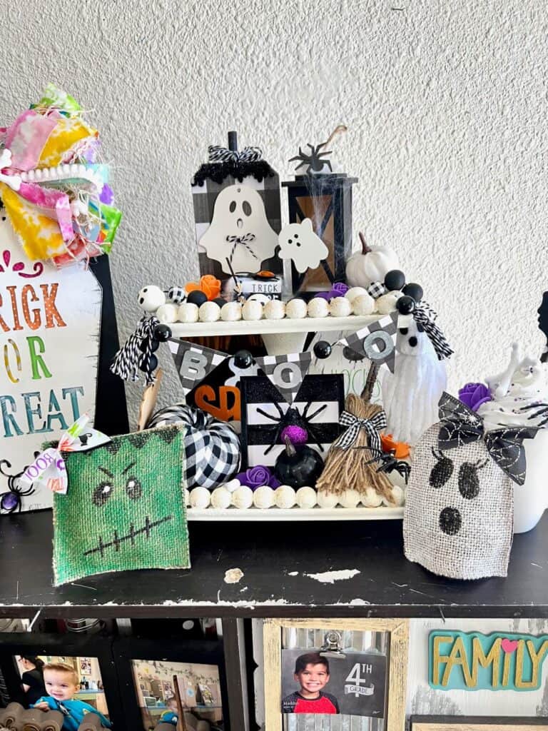 DIY Handmade Halloween Tiered Tray on a white wood bead 2 tiered tray with ghosts, spiders, witches broom, pumpkins, bones, frankenstien, mummy and other Halloween decor.
