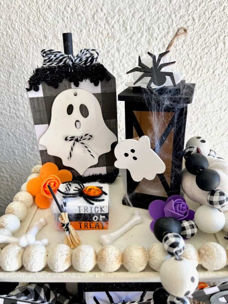 Black and white buffalo check ghost, ghost black lantern, a mini book stack, and a purple flower on the top of a tiered tray.