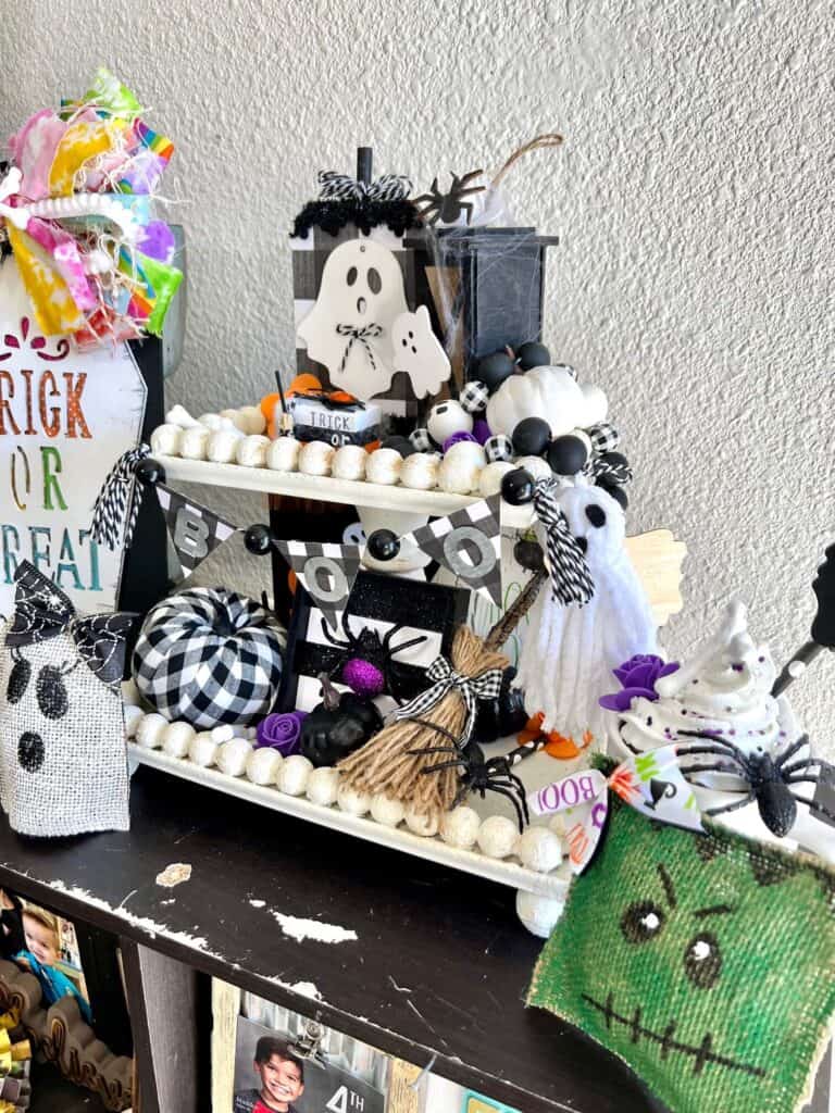 DIY Handmade Halloween Tiered Tray on a white wood bead 2 tiered tray with ghosts, spiders, witches broom, pumpkins, bones, Frankenstein, mummy and other Halloween decor.