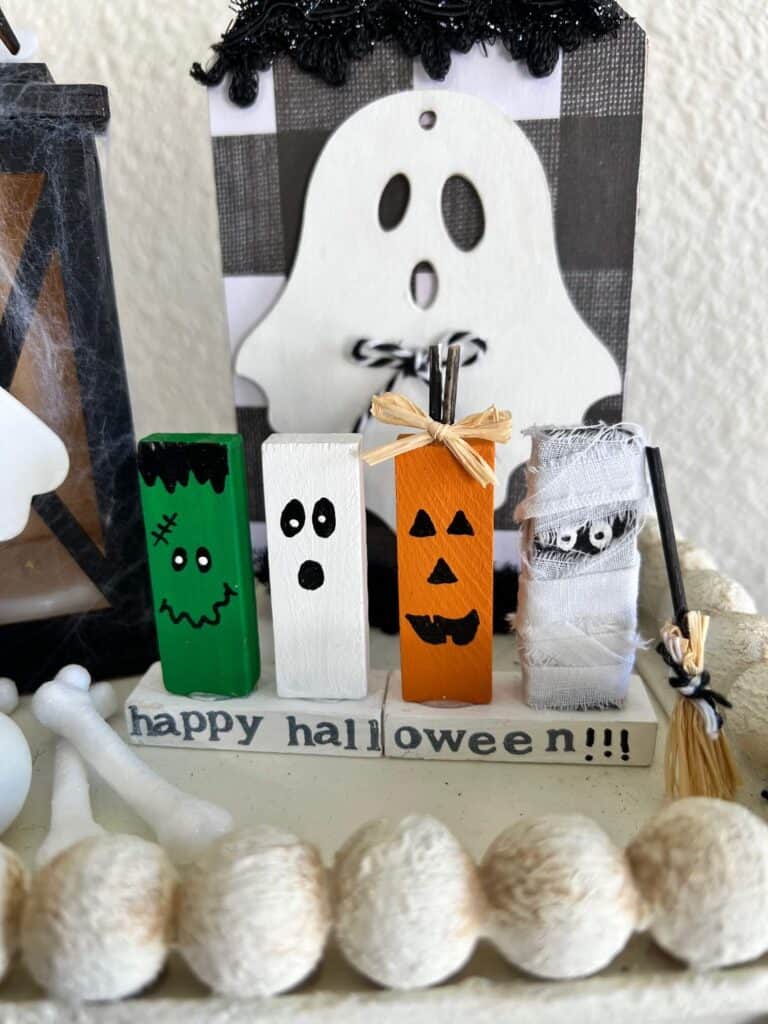 4 jenga block halloween characters on a stand. One Frankenstein, one Ghost, one Pumpkin, and one Mummy, that says "Happy Halloween" underneath.