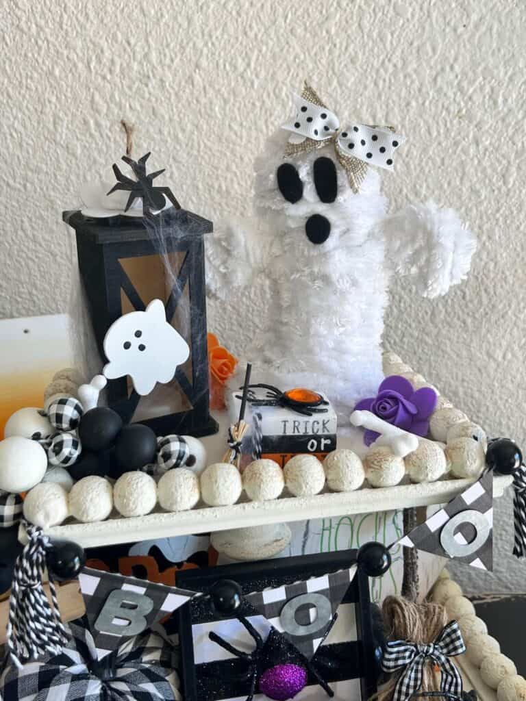 Black ghost lantern, white yarn wrapped ghost, and mini halloween book stack on the top of a white tiered tray.
