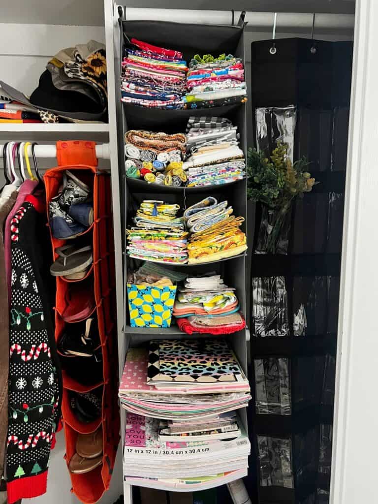 A hanging clothes organizer in a closet with all the shelves full of fabric and scrapbook paper.