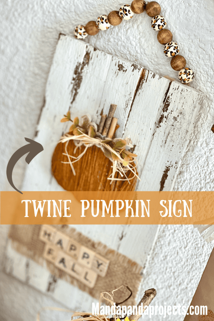 Rustic Happy Fall Twine Pumpkin Sign made on a wood shim chippy white background, cardboard orange twine pumpkin, leopard print wood bead hanger, and a burlap strip at the bottom that says "Happy Fall" in scrabble tile letters.