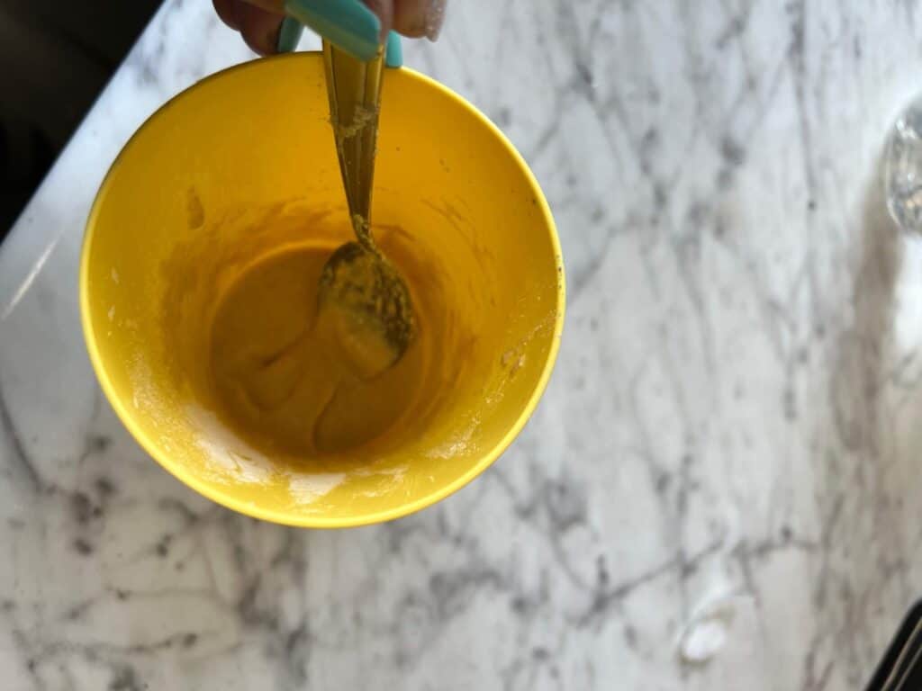 A yellow cup holding the paste of vinegar, salt, and flour with a spoon in it.