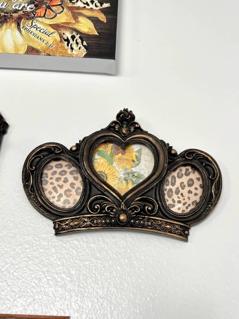 Thrift Store Crown Frame Makeover with black frame and gold rub n buff to make it look old and vintage and leopard print scrapbook paper along with sunflower rice paper inside the frame, hanging on a gallery wall.