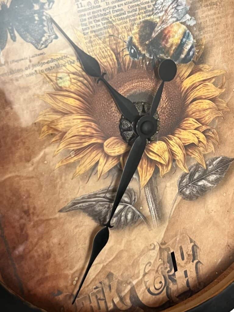 The front center of the clock showing the clock hands coming out of the center of the sunflower.