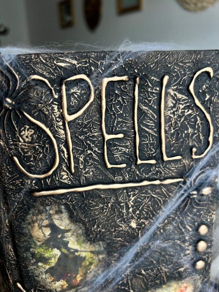 The words "SPELLS" spelled out in hot glue on the top of the book, with gold rubbed on top.