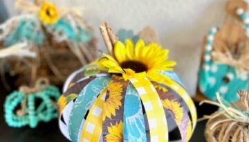 Scrapbook Paper Pumpkin made with a Toilet paper roll, teal, yellow, and brown sunflower scrapbook paper, sticks as a stem, a sunflower head, and a burlap leaf for simple recycled crafts DIY fall decor.