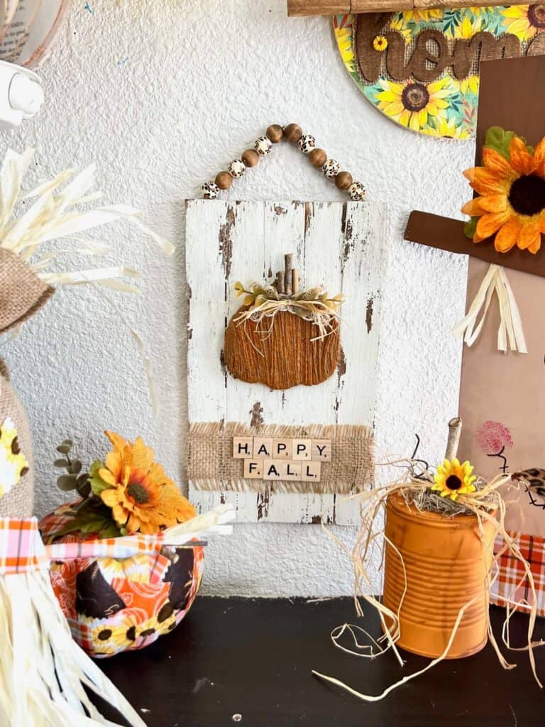 The completed pumpkin project hanging on the wall staged with other diy fall crafts and decor.