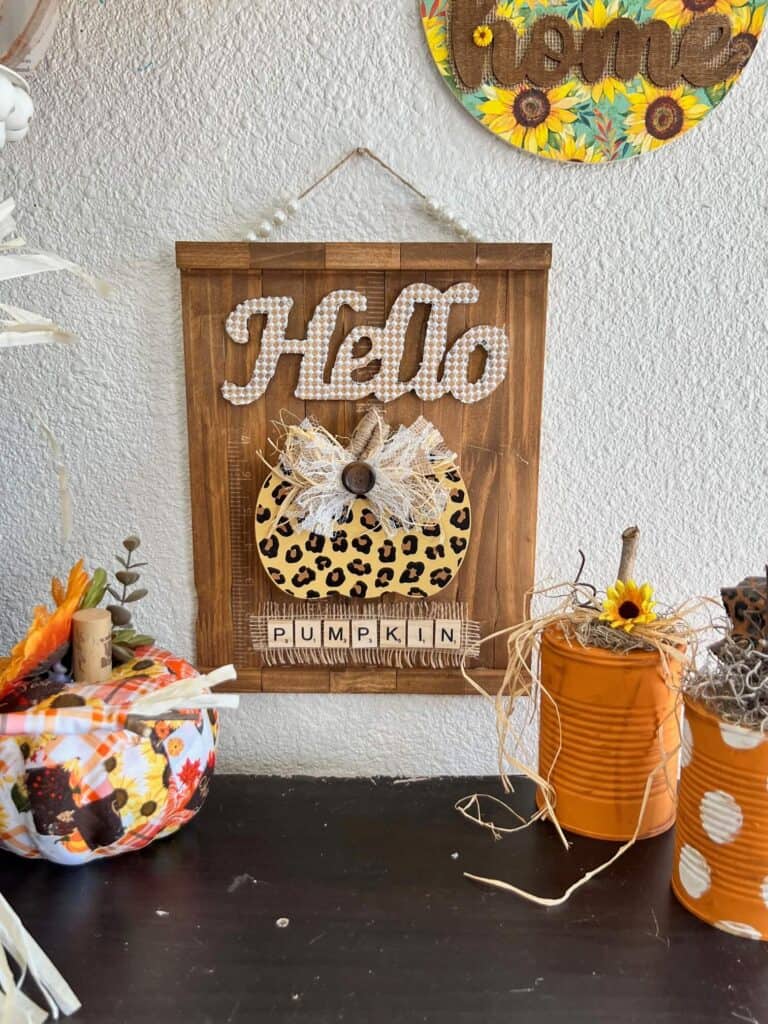 The completed leopard print pumpkin craft hanging on the wall with a bookcase full of diy fall crafts and decor underneath.