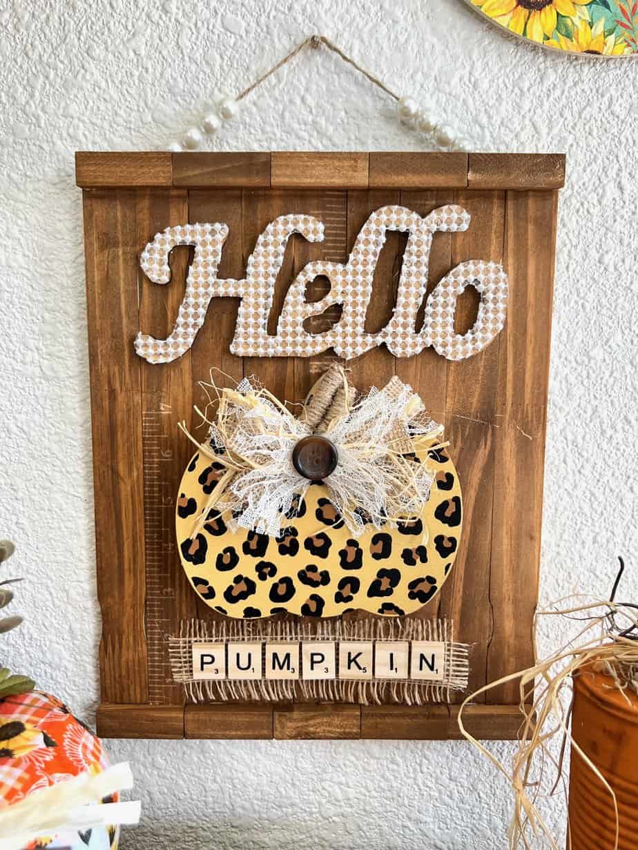 Hello leopard pumpkin DIY fall decor with a stained paint stick background, pearl bead hanger, lace and burlap bow, and scrabble tile letters.