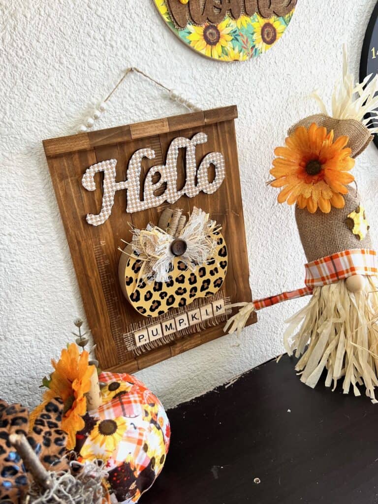 The completed Hello Pumpkin Sign hanging on the wall next to a scarecrow gnome and a patchwork pumpkin.