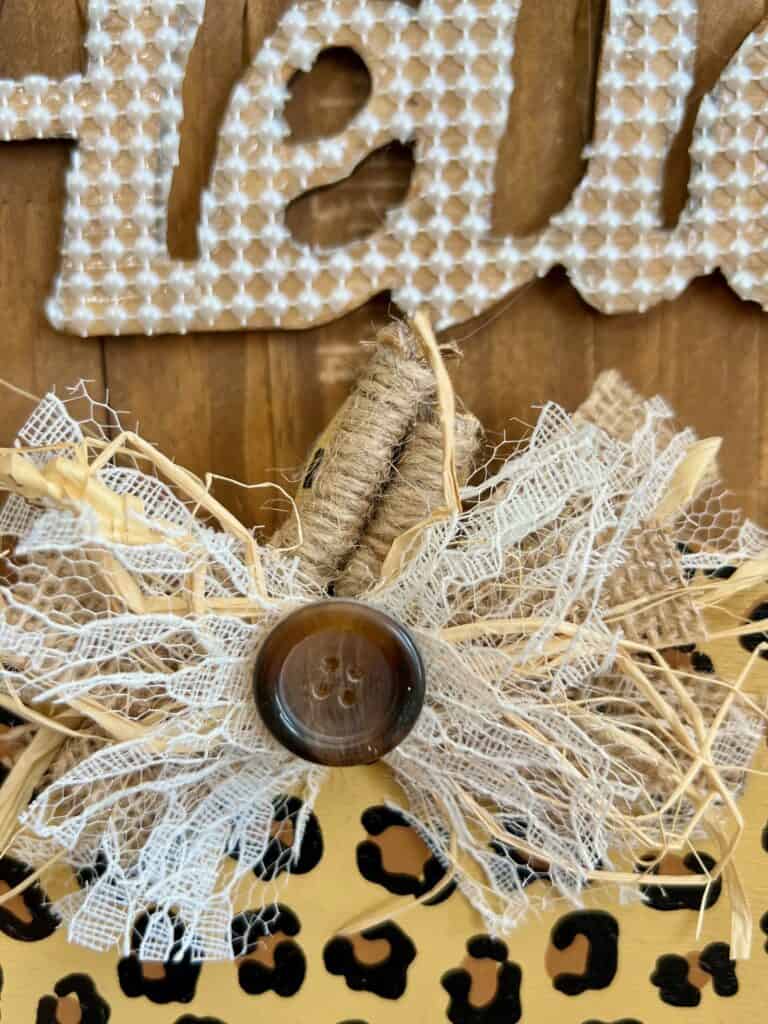 The lace burlap and raffia bow glued to the top of the pumpkin stem with a button in the center.