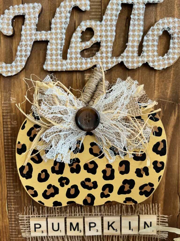 Leopard print wood pumpkin cutout with a lace and burlap bow on top and a twine covered stick as a stem.