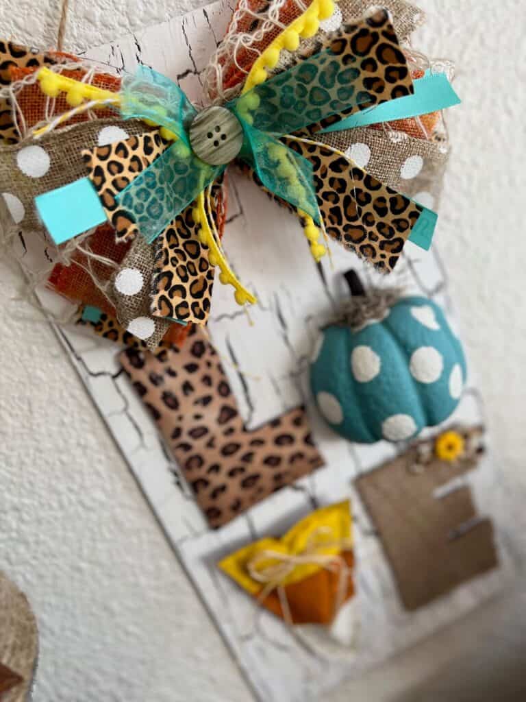 Big messy bow with yellow, orange, teal and leopard print with a button in the center, at the top of the project above where it says LOVE on the crackle background.