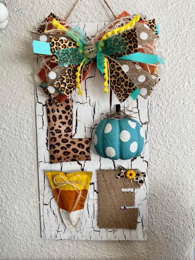 Fall in "LOVE" Door Hanger with the crackle paint white surface, leopard print L, teal polka dot pumpkin O, candy corn V, and burlap E, and big messy bow! DIY fall decor.