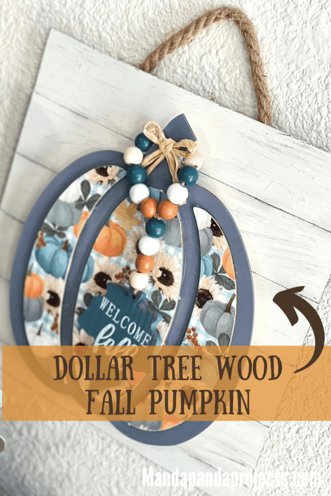 Dollar Tree Fall Wood Pumpkin Sign with a blue grey pumpkin with pretty fall scrapbook paper, a "welcome fall" leaf wood bead garland hanging from the Pumpkin stem, mounted on a faux shiplap background hanging with jute rope.