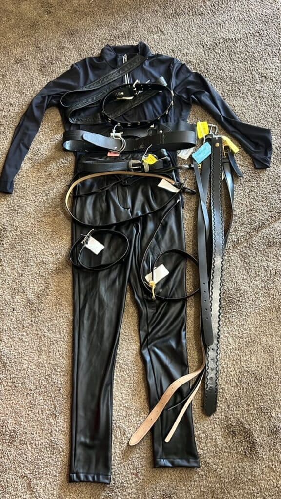 All of the thrift store clothes and belts laid out on the floor that will be used to make the black belted leather suit.