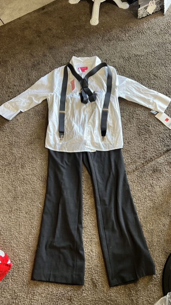 The thrift store clothes laid out on the floor to make the grey pants and the white shirt with suspenders outfit.