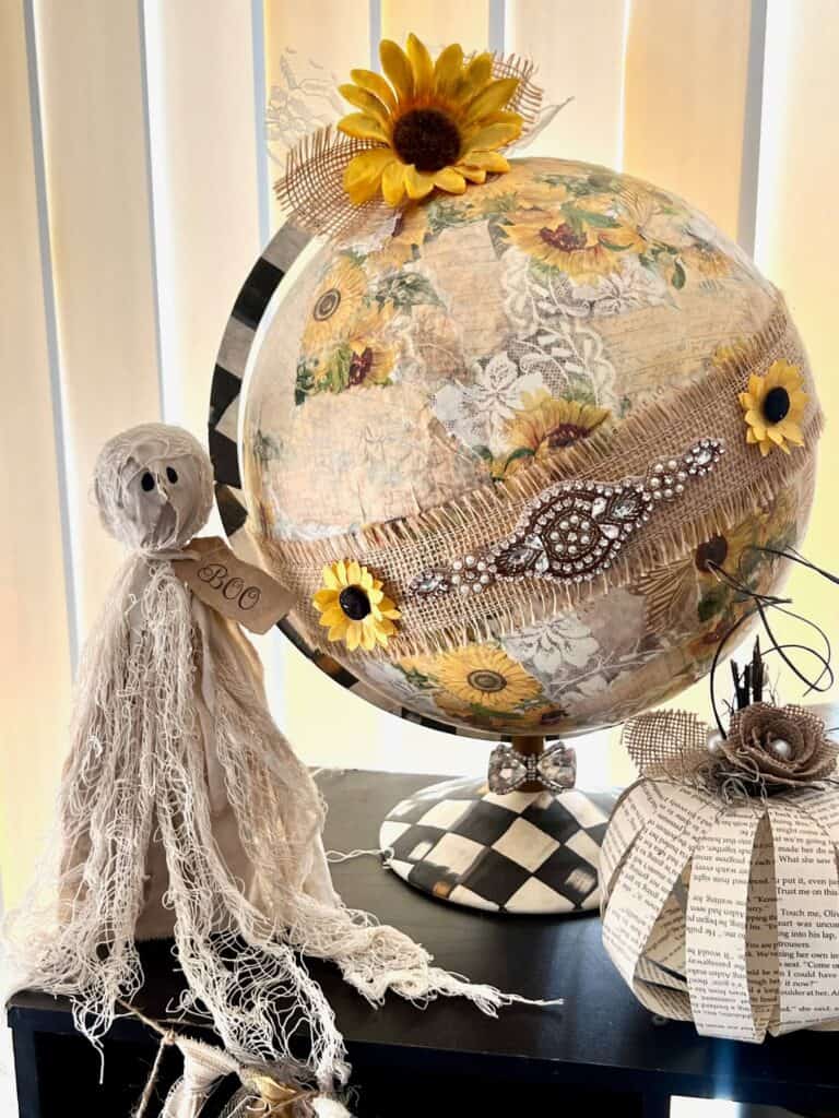 A primitive tattered ghost sitting on a bookcase next to a Sunflower Thrift Store globe upcycle.