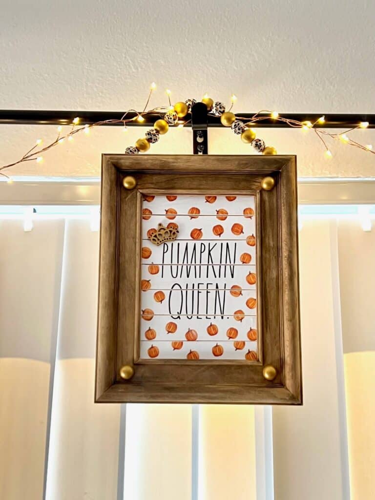 A reverse canvas frame with a napkin inside that says "Pumpkin Queen" and leopard and gold bead hanger.