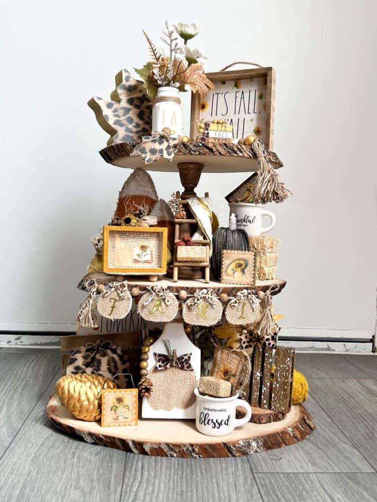 Neutral fall tiered tray with accents of leopard print, sunflowers, gold, and lots of pumpkins, acorns, pine cones, leaves, and other typical fall decor. Rustic handmade tiered tray with lots of handmade decor pieced on it to decorate for autumn and fall.