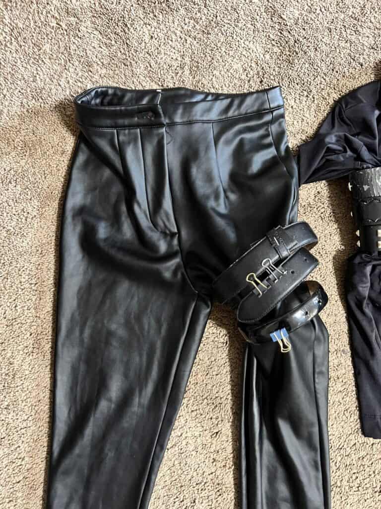 The black pleather pants on the floor with belts glued around the left leg.