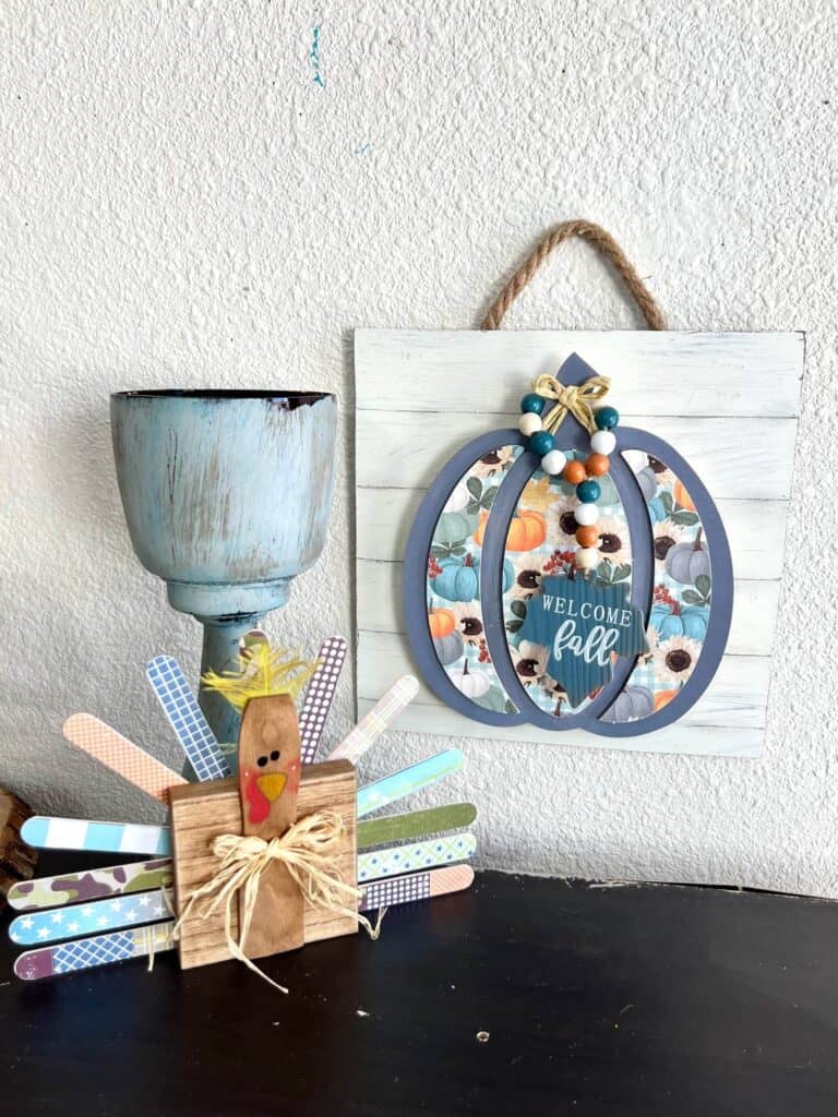 The 3d fall wood pumpkin decor hanging on the wall next to a chunky candlestick and a paint stick wood block turkey diy.