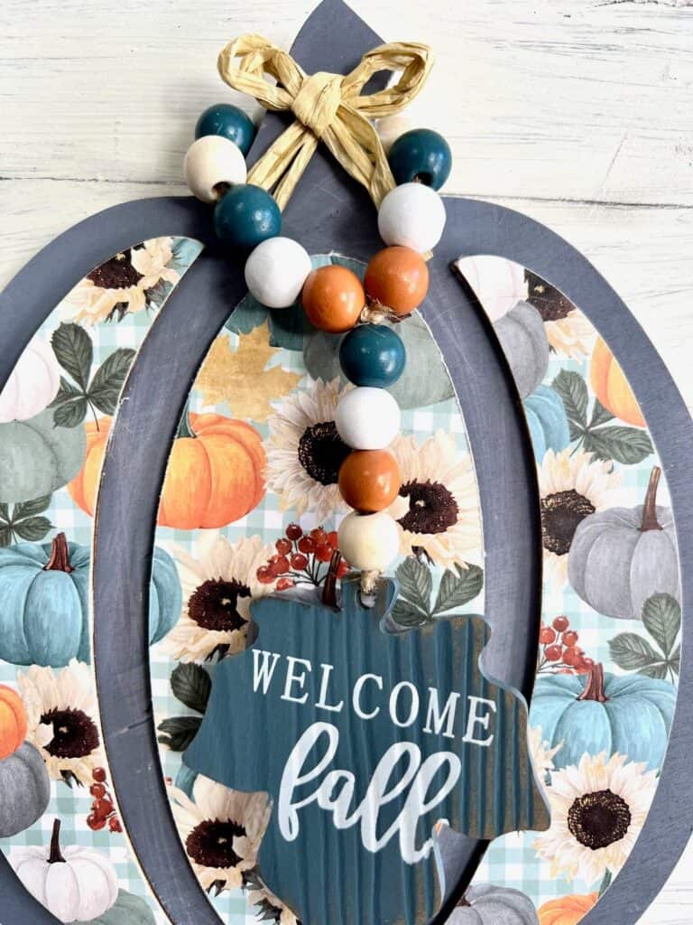 A "welcome fall" wood bead garland hanging from the wood pumpkin stem.