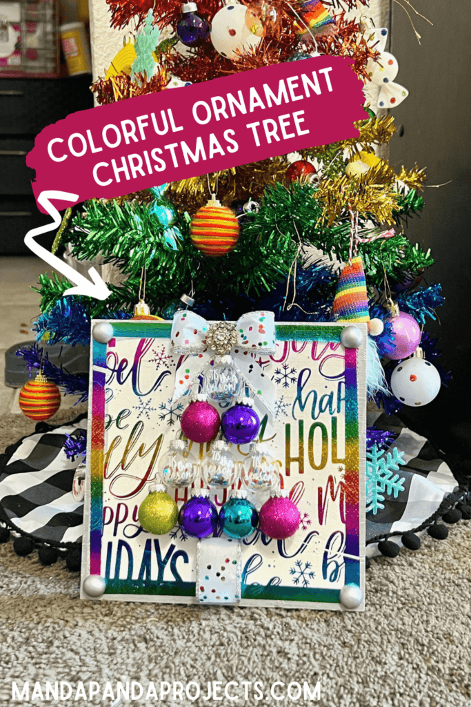 Colorful Ornament bulb Christmas Tree Frame made with a holiday rainbow color napkin with various christmas phrases on it, small round bulb ornaments in the shape of a christmas tree with a bow as the tree topper and som totally dazzled bling. Bright and cheery diy christmas decor.