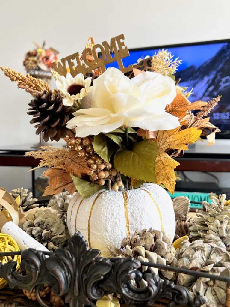 A dollar tree foam pumpkin painted white with gold lines, with neutral fall florals coming out the top and a "hello fall" pick, for a gorgeous and affordable thanksgiving table centerpiece and decor.