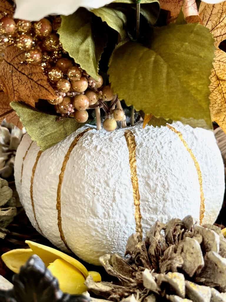 The bottom of the floral foam pumpkin centerpiece showing the pumpkin painted white with gold lines.