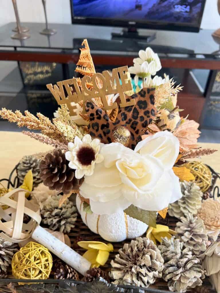 Top view of the floral pumpkin centerpiece showing all of the floral coming out of the top of the pumpkin, leopard print leaves, and a "hello fall" wood cutout pick.