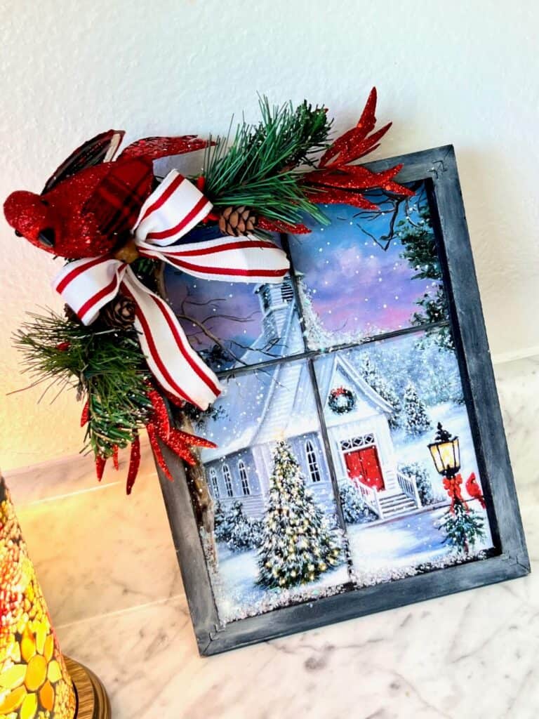 Christmas Church gift bag from walmart, turned into window winter scene with a reverse canvas and skewers, with greenery, a cardinal, and a bow in the corner. Easy DIY Christmas crafts and decor.