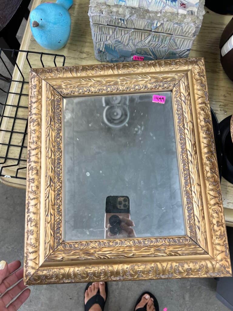Thrift store mirror with gold frame, sitting on a table at the thrift store.
