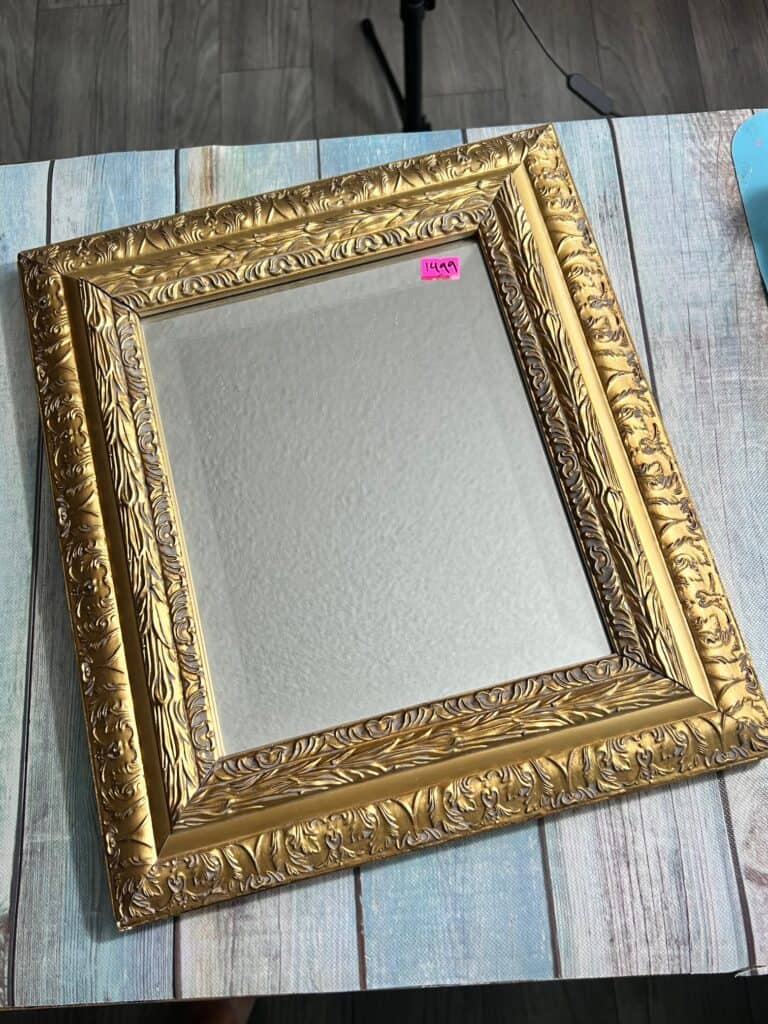Thrift store mirror with gold frame, sitting on a table.