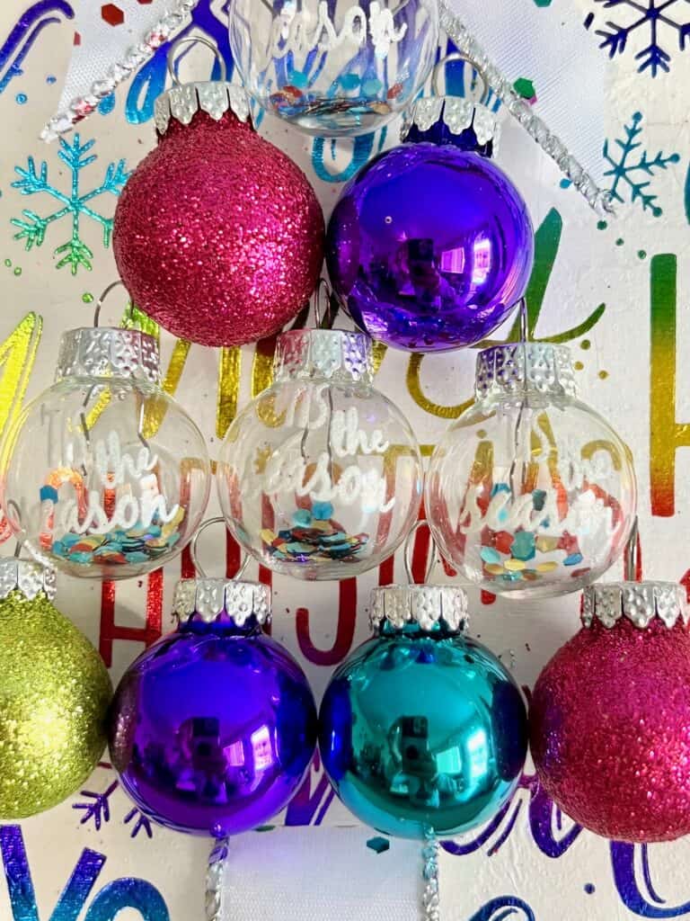 Close up of the small colorful ornament christmas bulbs used to build the christmas tree frame. They say "tis the season".