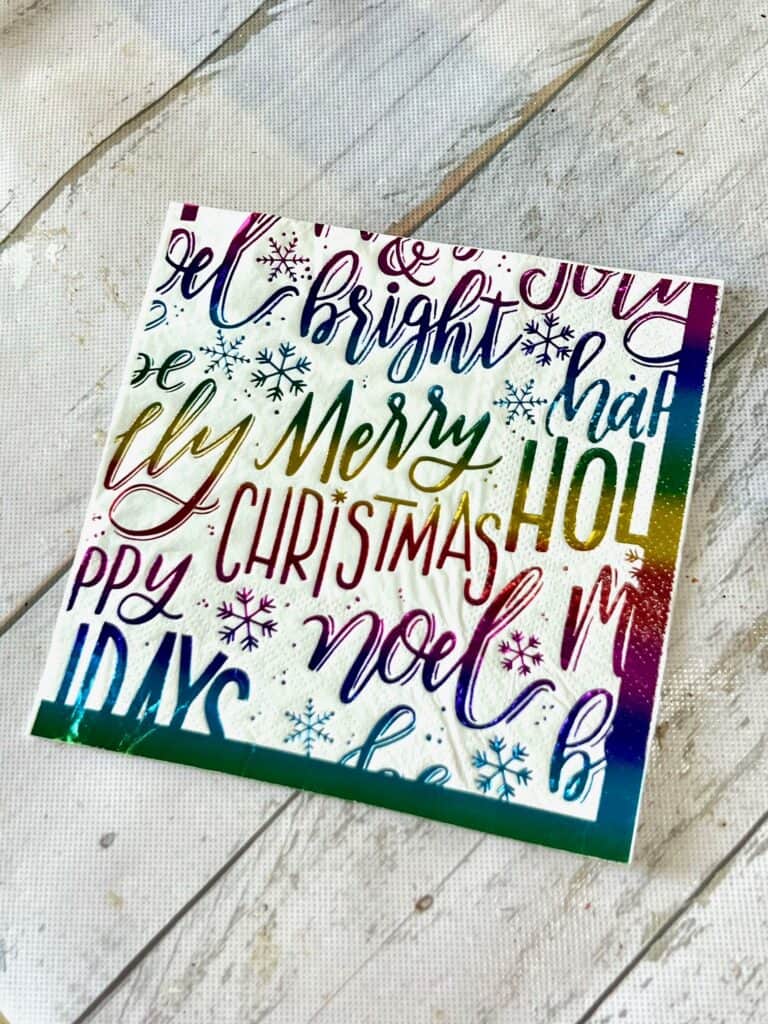 Colorful rainbow Christmas napkin with lots of holiday phrases and words written on it.
