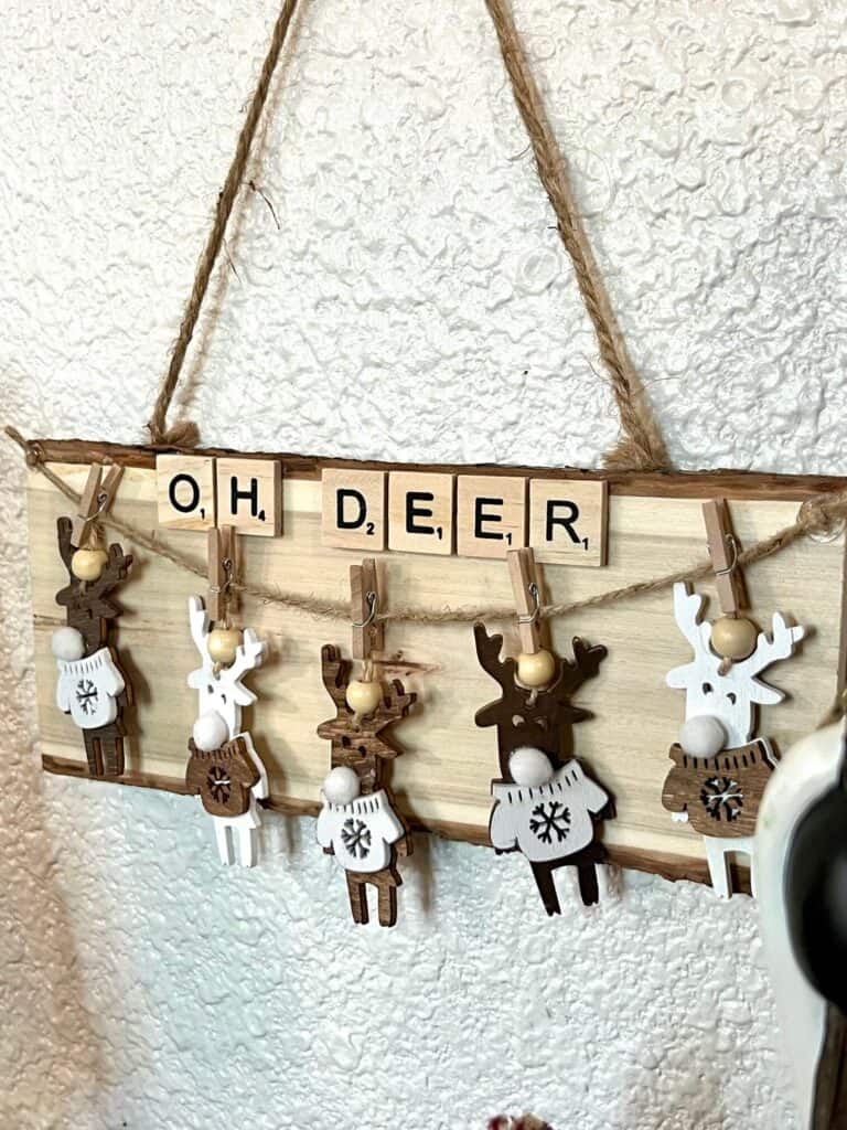 DIY Reindeer Oversized Christmas Ornament with 5 neutral tan deer, hanging from a piece of twine with mini clothespins and scrabble tile letters at the top that says "OH DEER"  all on a piece of Dollar Tree natural wood plaque.