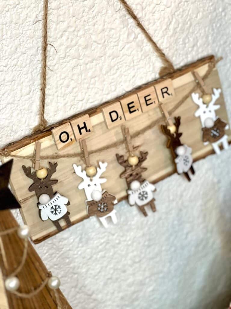 DIY Reindeer Oversized Christmas Ornament with 5 neutral tan deer, hanging from a piece of twine with mini clothespins and scrabble tile letters at the top that says "OH DEER"  all on a piece of Dollar Tree natural wood plaque.