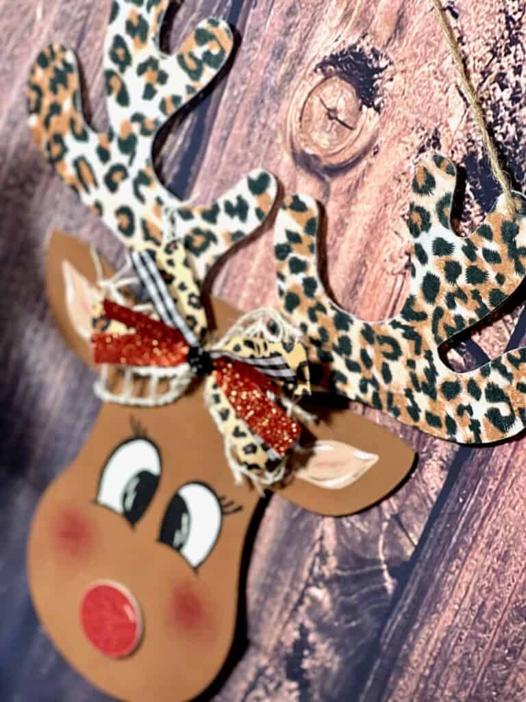 DIY Dollar Tree Wood Rudolph the Red Nosed Reindeer, with leopard print antlers, a hand painted face, and cute bow for DIY Christmas decor.