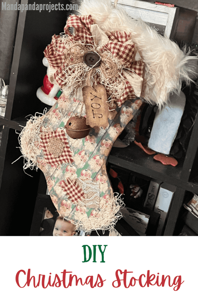 DIY Christmas Stocking made from cardboard with vintage red and green santa scrapbook paper, burlap patches, a messy fabric bow, a "joy" hangtag, a rusty bell, and grungy faux fur hanging with twine.