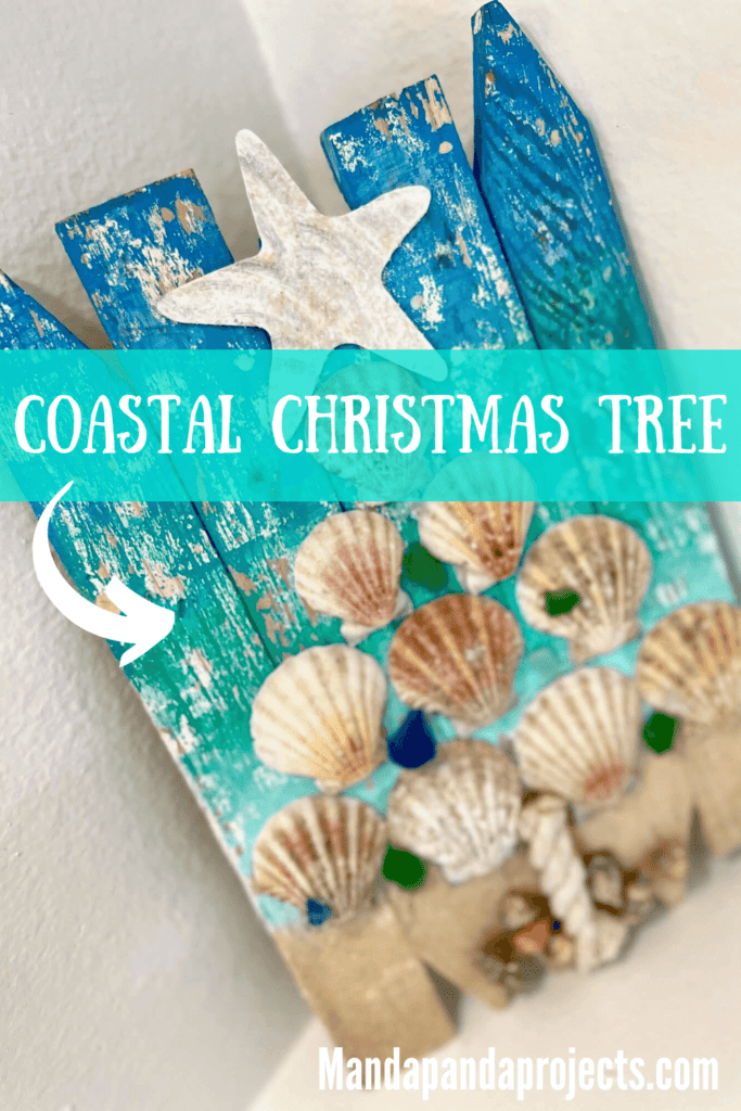 Seashell Coastal Christmas Tree with blue and green Ombre background, real sand and shells at the bottom, seashells in the shape of a Christmas tree, and a white sparkly starfish on top, with a nautical rope tree trunk. DIY coastal nautical Christmas in July decor.