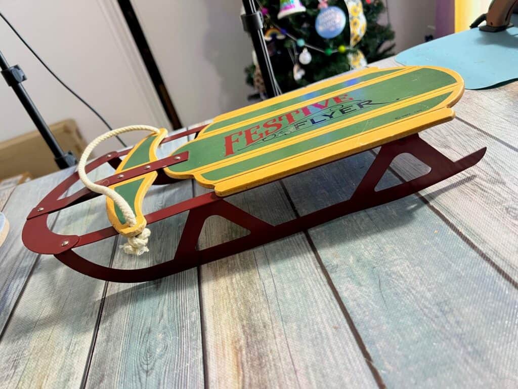 The thrift store wood sled that says "festive flyer" on it, sitting on a table.