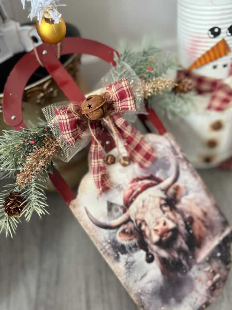 Thrift Store Christmas Highland Cow Sled Makeover with rice paper, greenery and berries and a bow with rusty bells. DIY Christmas decor made with a thrifted sled.