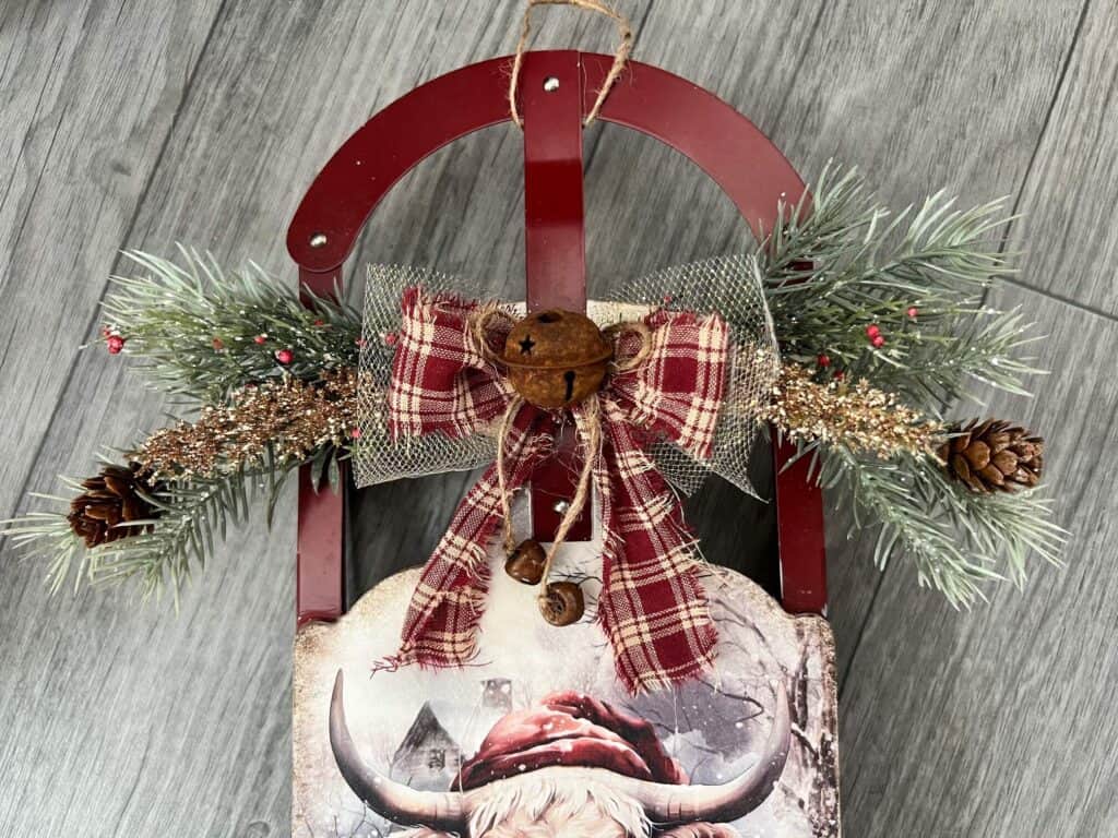 The top of the christmas sled with faux greenery and berries, a red fabric bow and rusty bells.