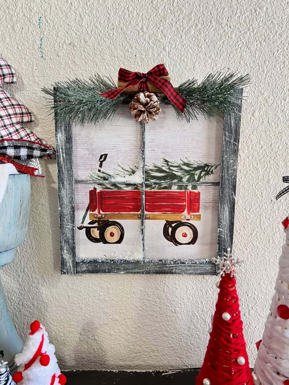 Christmas Wagon with a christmas tree in it Gift Bag Window Frame with black painted paint sticks as the frame, dry brushed with white to look like snow, faux snow, snowy greenery at the top with cinnamon sticks, a pine cone, and a black and red buffalo check bow.