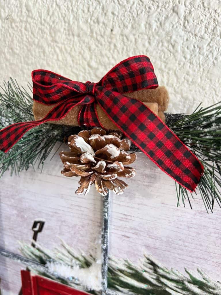 The top of the project with faux pine greenery, a small pine cone, cinnamon sticks and a black and red buffalo check bow.