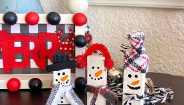 Jenga Block Snowmen made with Dollar Tree tumbling tower blocks, painted white with simple hand drawn faces, and decorated with fabric and twine scarves, hats, top hats, and ear muffs to display on your Christmas and winter themed DIY tiered trays.