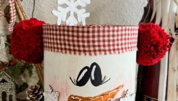 Coffee can snowman made with a recycled coffee can, rusty wire, red pom pom ear muffs, a hand painted face, snowflakes and a hangtag that says "Feeling frosty" for DIY christmas and winter crafts and decor.
